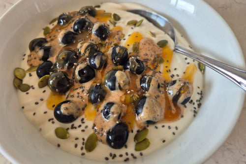 Yogurt bowl with blueberries, honey, and seeds on a white plate.