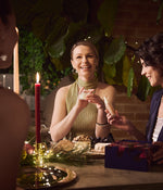 Two women sitting at a table with candles and food, one is holding a Manuka Health skincare gift box.