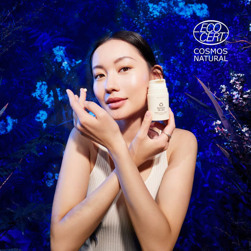 Woman applying cream to her face with a blue floral background and EcoCert Cosmos Natural logo.