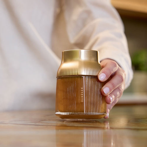 Hand holding Manuka Health's Reserve MGO 1000+ glass jar with gold cap. 