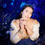Woman holding a Manuka Health Eternal Renewal Nourishing Lip Balm against a dark, floral background.